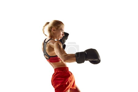 Téléchargez les photos : Jeune femme musclée, athlète de boxe en mouvement, pratiquant des coups isolés sur fond blanc. Concept de sport, mode de vie actif et sain, force et endurance, soins corporels - en image libre de droit