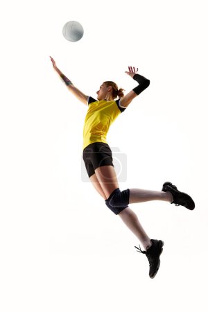 Téléchargez les photos : Image dynamique complète de la jeune femme, joueuse de volley-ball en mouvement, pratiquant, frappant balle en saut isolé sur fond blanc. Concept de sport, compétition, mode de vie actif et sain, passe-temps - en image libre de droit
