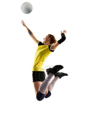 Téléchargez les photos : Jeune femme, joueuse professionnelle de volley-ball en uniforme jaune noir, frappant la balle dans un saut isolé sur fond blanc. Concept de sport, compétition, mode de vie actif et sain, passe-temps - en image libre de droit