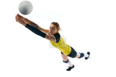 Téléchargez les photos : Jeune femme compétitive dynamique, joueuse de volley-ball en mouvement pendant le match, frappant balle isolée sur fond blanc. Concept de sport, compétition, mode de vie actif et sain, passe-temps - en image libre de droit