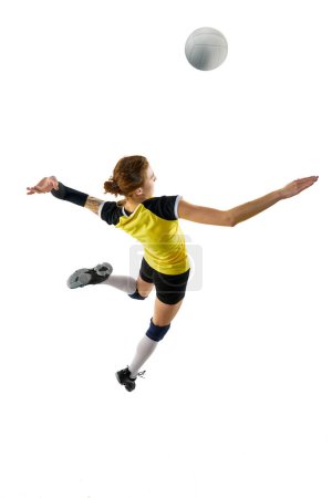 Téléchargez les photos : Jeune femme, joueuse professionnelle de volley-ball en uniforme jaune noir, frappant la balle dans un saut isolé sur fond blanc. Concept de sport, compétition, mode de vie actif et sain. Vue du dessus - en image libre de droit