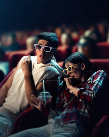 Téléchargez les photos : Jeune homme et femme émotionnel portant des lunettes 3D, assis au cinéma et regardant un film d'horreur. Des émotions de peur. Concept de temps libre, relation, émotions, activité de week-end - en image libre de droit