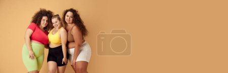 Foto de Sonriendo hermosa mujer sobrepeso en ropa deportiva de pie sobre fondo de estudio beige. Concepto de deporte, positividad corporal, pérdida de peso, cuidado corporal y de la salud. Banner. Espacio vacío para insertar texto - Imagen libre de derechos