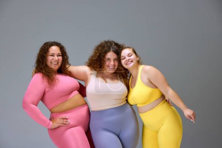 Photo for Support. Three beautiful women with oversized bodies, wearing sportswear, posing against grey studio background. Concept of sport, body-positivity, weight loss, body and health care - Royalty Free Image