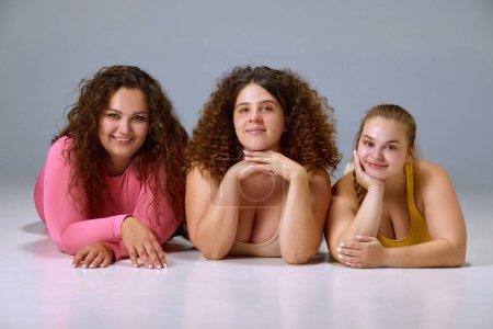 Foto de Belleza natural. Retrato de mujeres jóvenes sonrientes, además de modelos de tamaño posando sobre fondo gris estudio. Concepto de deporte, positividad corporal, pérdida de peso, cuidado corporal y de la salud - Imagen libre de derechos