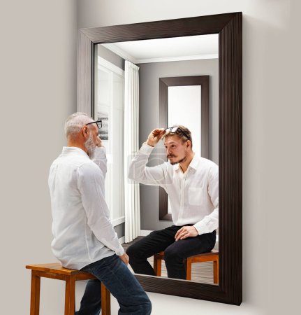 Photo for Revealing past memories. Senior man looking in mirror at his younger reflection. Through ages. Conceptual collage. Concept of present, past and future, age, life cycle, generation, ad - Royalty Free Image