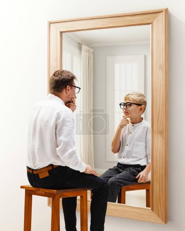 Photo for Man in formal wear sitting and looking in mirror with reflection of him being a child. Dreams and reality. Conceptual collage. Concept of present, past and future, age, life cycle, generation, ad - Royalty Free Image