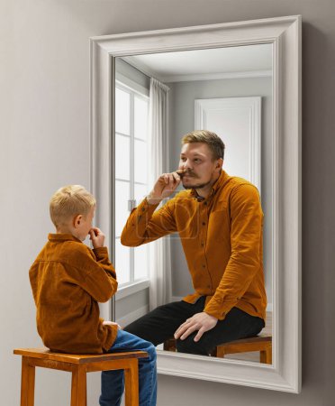 Photo for Little boy, child sitting near mirror and dreaming, imagining him being adult man. Conceptual collage. Concept of present, past and future, age, life cycle, generation, ad - Royalty Free Image