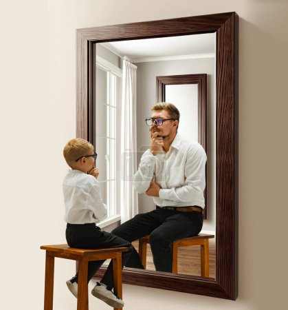 Téléchargez les photos : Petit garçon, enfant assis près du miroir et imaginant qu'il était un homme adulte. Je pense à l'avenir. Collage conceptuel. Concept de présent, passé et futur, âge, cycle de vie, génération, publicité - en image libre de droit
