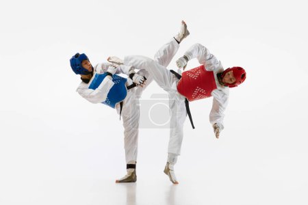 Photo for Dynamic image of young men, taekwondo athletes in kimono and helmets training isolated over white background. Concept of martial arts, combat sport, competition, action, strength, education - Royalty Free Image