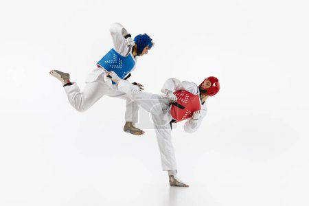 Photo for Dynamic image of young men, taekwondo athletes in kimono and helmets training isolated over white background. Concept of martial arts, combat sport, competition, action, strength, education - Royalty Free Image