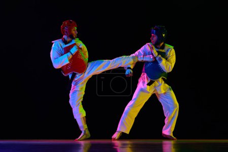 Photo for Athletic, strong young men, taekwondo athletes in motion, fighting, training against black background in neon light. Concept of martial arts, combat sport, competition, action, strength - Royalty Free Image