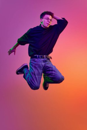 Photo for Young man in casual stylish clothes and eyeglasses jumping with positive face against gradient pink background in neon light. Concept of human emotions, youth, delightful, excitement - Royalty Free Image