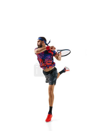 Téléchargez les photos : Image dynamique complète de l'homme barbu athlétique, joueur de tennis en mouvement, pratiquant, jouant isolé sur fond blanc. Concept de sport professionnel, mouvement, compétition, action. Publicité - en image libre de droit