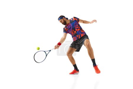 Téléchargez les photos : Homme barbu dans la trentaine, tennis en uniforme coloré pratiquant, balle de retour avec raquette isolée sur fond blanc. Concept de sport professionnel, mouvement, compétition, action. Publicité - en image libre de droit