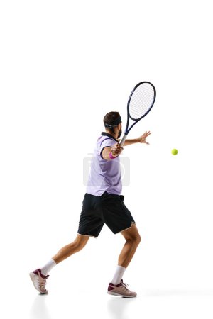 Téléchargez les photos : Homme, joueur de tennis en mouvement pendant le jeu, l'entraînement, frapper la balle avec raquette isolé sur fond blanc. Concept de sport professionnel, mouvement, compétition, action. Publicité - en image libre de droit