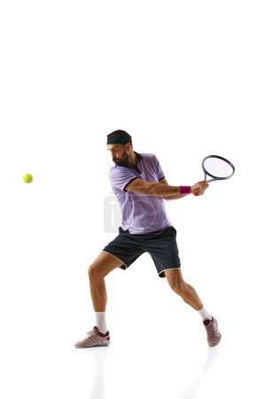 Téléchargez les photos : Jeune homme compétitif concentré, joueur de tennis en mouvement pendant le match, jouant isolé sur fond blanc. Concept de sport professionnel, mouvement, compétition, action. Publicité - en image libre de droit