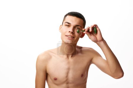 Photo for Handsome young shirtless man doing face massage with special tool - roller against white studio background. Lifting effect. Concept of male beauty, skin care, spa, cosmetology, mens health - Royalty Free Image