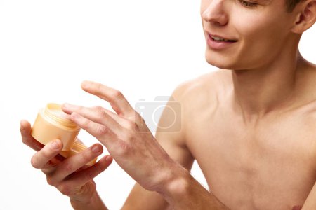 Foto de Imagen recortada de un hombre joven sin camisa sosteniendo tarro con crema hidratante sobre fondo blanco del estudio. Concepto de belleza masculina, cuidado de la piel, spa, cosmetología, salud de los hombres - Imagen libre de derechos
