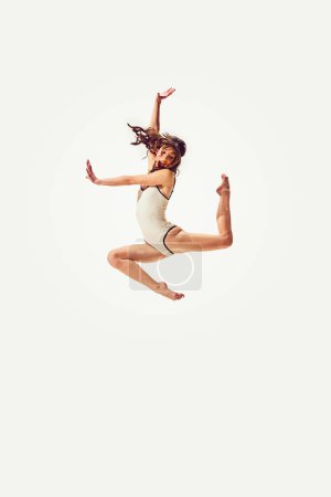 Foto de Hermosa mujer joven en traje de baño vintage con estilo saltando alegremente sobre fondo blanco. Buceando en el agua. Diversión y alegría. Concepto de vacaciones de verano, viajes, estilo retro, moda - Imagen libre de derechos