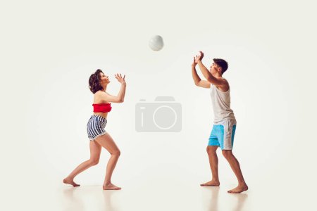 Foto de Jóvenes, hombres y mujeres, amigos jugando voleibol de playa, divirtiéndose en balneario sobre fondo blanco. Concepto de vacaciones de verano, viajes, estilo retro, moda, ocio - Imagen libre de derechos