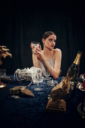 Foto de Retrato de una hermosa mujer joven en vestido elegante sosteniendo la copa con champán, asistiendo a la cena misteriosa. Navidad, celebración de Año Nuevo. Concepto de estilo de vida de lujo, belleza, evento, moda - Imagen libre de derechos