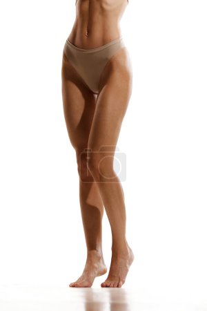 Photo for Cropped image of slender, tanned, smooth female legs. Model posing in beige cotton underwear against white studio background. Concept of female beauty, body and skin care, depilation, epilation - Royalty Free Image