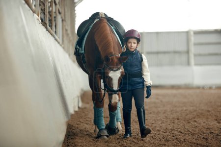 Foto de Niña, niño con uniforme especial y casco caminando con caballo durante el curso educativo de equitación. Comportamiento y cuidado animal. Deporte, infancia, escuela, estilo de vida activo, concepto de hobby - Imagen libre de derechos