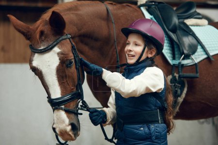 Foto de Niña, niña con casco cuidando a caballo, mostrando su amor. Entrenamiento infantil a caballo en arena especial, pabellón. Concepto de deporte, infancia, escuela, curso, estilo de vida activo, hobby - Imagen libre de derechos