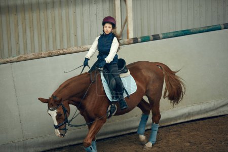 Photo for Concentrated little girl in inform and special clothes siting on horse, training horseback riding on special manege. Concept of sport, childhood, school, course, active lifestyle, hobby - Royalty Free Image