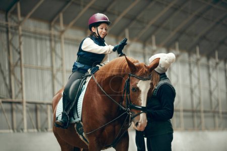 Photo for Good lesson,. Little girl giving high five to her instructor. Learning horseback riding on special arena. Concept of sport, childhood, school, course, active lifestyle, hobby - Royalty Free Image