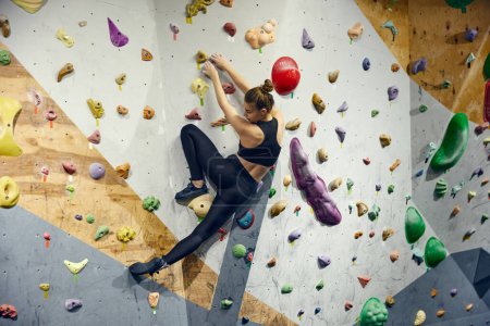 Photo for Sportive young woman in sportswear, training bouldering activity, climbing wall, practicing. Indoor training class. Concept of sport, sport climbing, hobby, active lifestyle, school, training course - Royalty Free Image