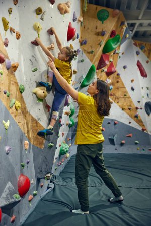 Photo for Little girl, child training with instructor, practicing bouldering activity, techniques. Little girl climbing wall, indoor class. Concept of sport climbing, hobby, active lifestyle, school, course - Royalty Free Image