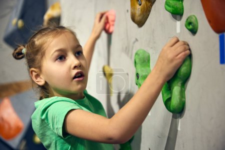 Photo for L:ittle girl, child attending bouldering course, training, climbing wall indoors. Sport education. Concept of bouldering, sport climbing, hobby and active lifestyle, school, training course - Royalty Free Image