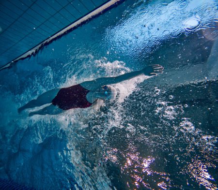 Photo for Bubbles. Young woman in swimsuit, cap and goggles training, practicing, swimming in pool indoors. Concept of pool sports, water sport, competition, active lifestyle - Royalty Free Image