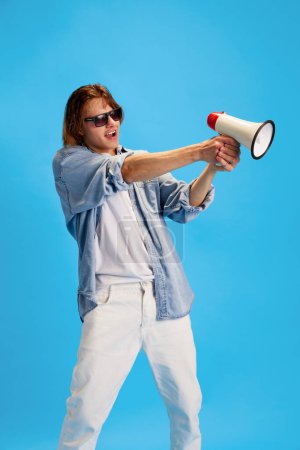 Photo for Information knight. Young man holds megaphone in his hands as weapon of truth against blue studio background. Concept of communication and media, sales season, shopping, information. Ad - Royalty Free Image