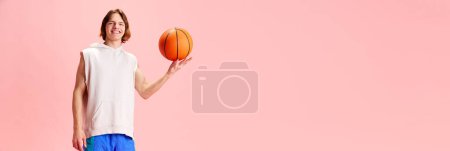 Foto de Deportista,, joven jugador de baloncesto vestido uniforme retro y gira bola en un dedo sobre fondo rosa con espacio negativo para insertar texto. Concepto de estilo de vida activo, deporte, recreación, hobby - Imagen libre de derechos