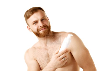 Photo for Red head, handsome young man with beard holding cosmetic product in hand. Male model looks well-groomed and healthy. Concept of natural beauty, youth, spa treatment, selfcare, cosmetic. Ad - Royalty Free Image
