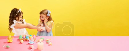 Photo for Little girl presenting to her friend a gift, box, Easter present against yellow background. Concept of Easter holiday, celebration, traditions, childhood, happiness. Banner. Empty space to insert text - Royalty Free Image