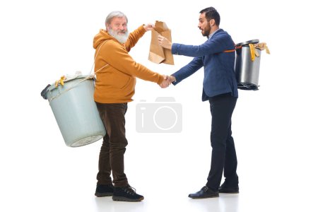 Foto de Sénior y hombre de unos 30 años sosteniendo papeleras en la espalda, dándose la mano, limpiando basura aislada sobre fondo blanco. Concepto de medio ambiente, ecología, cuidado de la naturaleza, reciclaje, sensibilización - Imagen libre de derechos