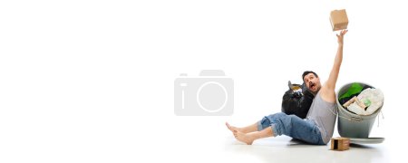 Téléchargez les photos : Jeune homme pieds nus couché avec des ordures et poubelle isolé sur fond blanc. Concept d'environnement, écologie, protection de la nature, recyclage, sensibilisation - en image libre de droit