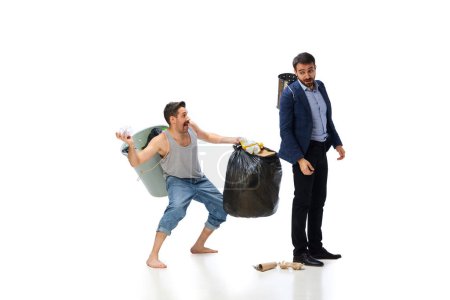 Téléchargez les photos : Homme aux pieds nus portant poubelle, ramassant des ordures avec un homme d'affaires marchant isolé sur fond blanc. Concept d'environnement, écologie, protection de la nature, recyclage, sensibilisation - en image libre de droit