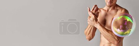 Foto de Imagen recortada de cuerpo masculino sin camisa muscular, manos fuertes en relieve con burbuja de jabón que maximiza la parte del cuerpo contra el fondo gris. Concepto de belleza masculina, pérdida de peso, dieta, salud. Banner - Imagen libre de derechos