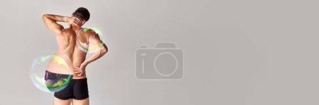 Téléchargez les photos : Vue arrière de l'homme torse nu musclé en caleçon, sous-vêtements, avec bulle de savon maximisant la partie du corps sur fond gris. Maux de dos. Concept de beauté masculine, perte de poids, régime alimentaire, santé. Bannière - en image libre de droit