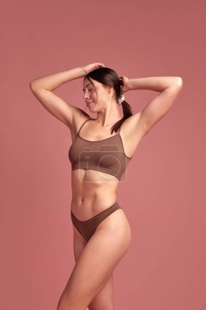 Photo for Happiness and wellness. Beautiful brunette young woman with slim healthy body standing in cozy cotton underwear over pink background. Concept of natural beauty, health and body care, body-positivity - Royalty Free Image