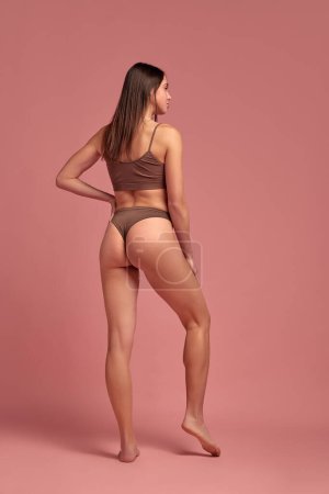 Photo for Weight-loss and anti-cellulite care. Full-length image of slim young woman standing in underwear against pinks studio background. Concept of natural beauty, health and body care, sport, diet, spa - Royalty Free Image