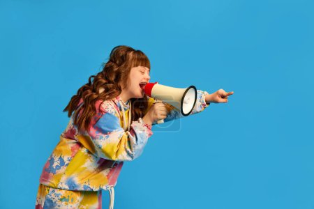 Photo for Health care awareness. Teen girl with down syndrome shouting in megaphone against blue studio background. Concept of acceptance, care, inclusion, health, diversity, emotions, social programs - Royalty Free Image