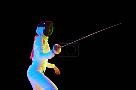 Photo for Female fencer, athlete in full uniform training, competing, practicing over black background in neon light. Concept of professional sport, competition, championship, hobby - Royalty Free Image