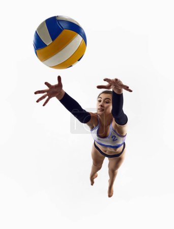Téléchargez les photos : Vue de dessus. Image dynamique d'une joueuse de volley-ball sportive en mouvement, pratiquant, sautant avec une balle isolée sur fond de studio blanc. Concept de sport professionnel, compétition, match, force - en image libre de droit