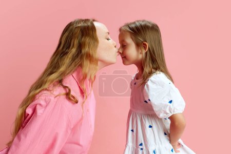 Foto de Querida maternidad. Madre cariñosa y cariñosa besando la nariz de sus hijas pequeñas contra el fondo rosa del estudio. Apoyo y amor. Concepto del Día de las Madres, Día Internacional de la Felicidad, paternidad - Imagen libre de derechos